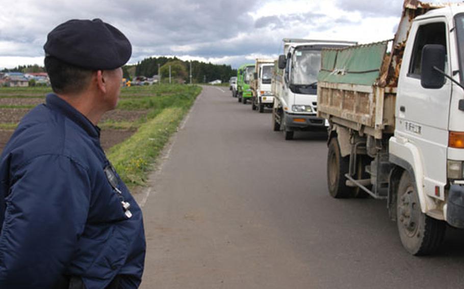 A Japanese national guard watches as delivery trucks head toward the Kamakita Gate at Misawa Air Base, Japan. The gate was opened after Pacific Air Forces mandated that all delivery and construction vehicles, 3/4-ton and heavier, be inspected upon entering Air Force bases in the Pacific.