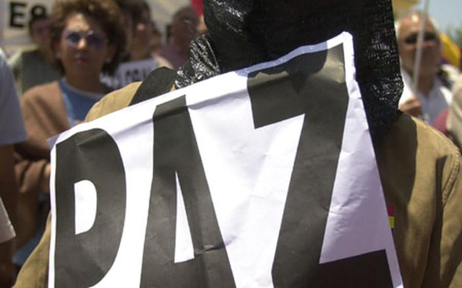 A protester on Sunday outside Naval Station Rota, Spain, holds a sign with "Paz" — the Spanish word for peace — while wearing a hood in protest of the Iraqi prisoner abuse scandal.