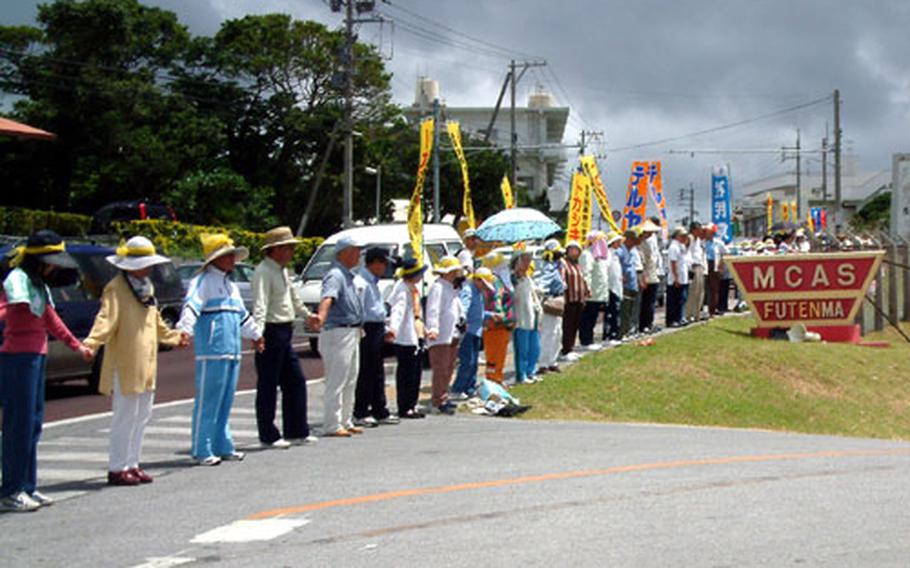 Protesters in front of a gate to MCAS Futenma hold hands during one of three successful rings around the air station Sunday during a demonstration observing the 32nd anniversary of Okinawa&#39;s reversion to Japan after World War II. Organizers say some 16,000 people particpated in the anti-base protest.