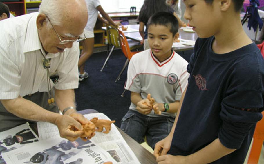 Alex Reid, left, and Stephen Shampine, 5th graders at Stearley Heights Elementary School, watch Mitsuyoshi Ikei show them how to put a final touch on their clay Wednesday during a special art class. Students at the elementary school participated in Shi-Shi making, an event the school celebrates for Asia Pacific Heritage Month.