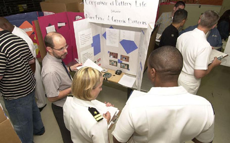 Educational Technology instructor, Gary Starrine (left), Lt. Rachel Spollen (center), and Petty Officer 1st Class Byron Stipe (right), from the Naval Pacific Meteorology and Oceanography Center judge a science project on the Comparison of Battery Life at Nile C. Kinnick High School Science Fair at Yokosuka Naval Base Friday.