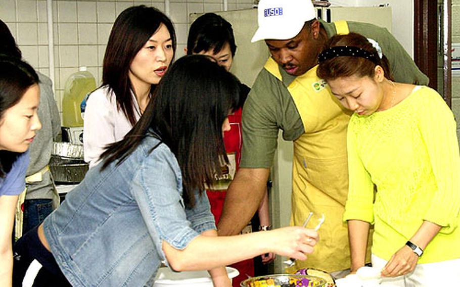 Marvin Sanders, center, walks a group of new brides through the cooking portion of the USO&#39;s Cross-Cultural School at Camp Kim, South Korea.