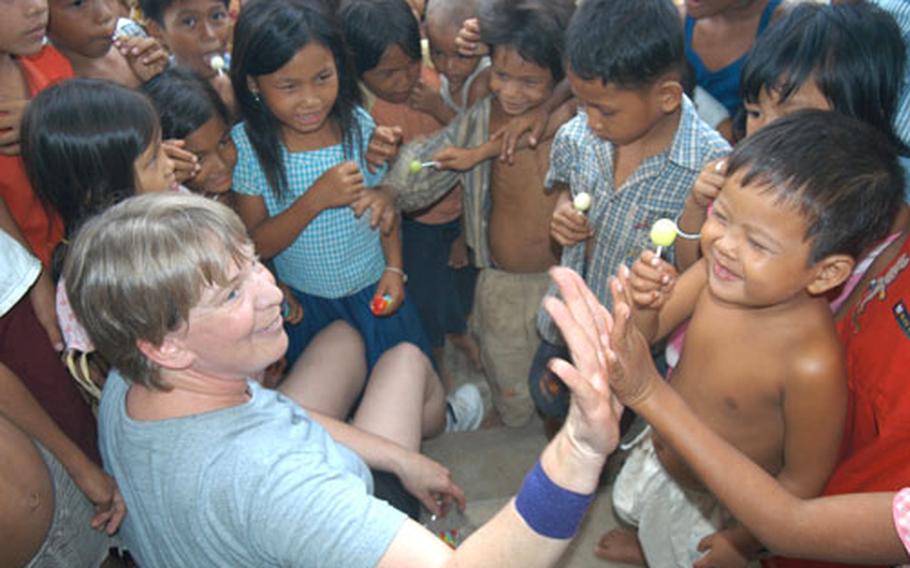 Air Force Master Sgt. Rita Greiner gives a high five after handing out a lollipop to a Cambodian boy as a pack of Cambodian children she&#39;s become a surrogate mother to gather around in a hospital compound in Kep.