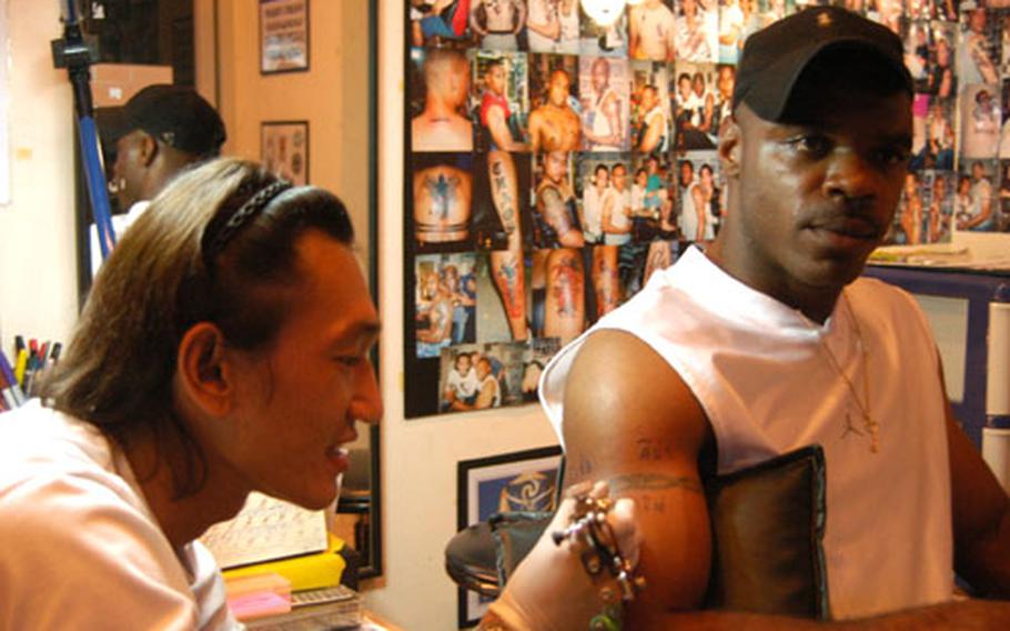 Tattooist Alex inspects a piece of work on the arm of Gunnery Mate 1st Class Jermaine White in Korat, Thailand. Alex, like many Thai tattoo artists, goes by only one name.