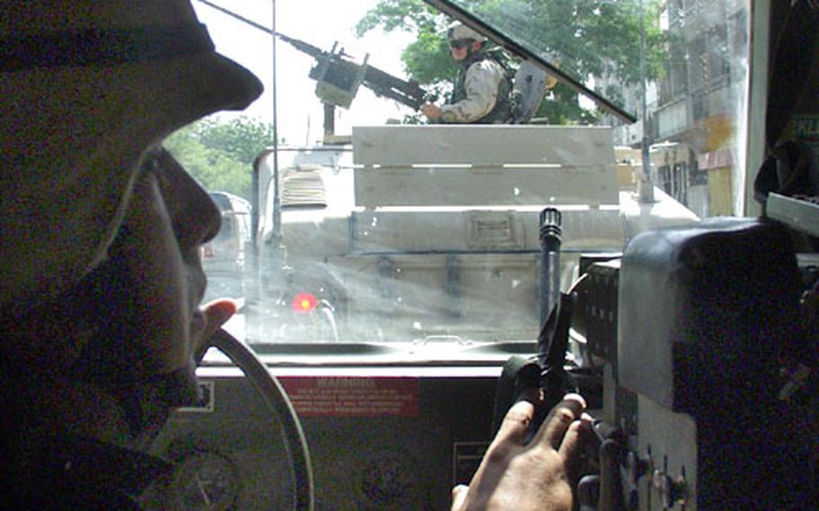 Sgt. 1st Class Luis Arroyo of Ocean Township, N.J., and the 759th Military Police Battalion, 39th Brigade Combat Team, drives the third Humvee of a four-vehicle convoy down Haifa Street in the Sunni section of Baghdad. His right hand steadies an M-16 automatic rifle. In the convoy ahead, Staff Sgt. Chris Pack of Orlando, Miss., 1st Battalion, 206th Field Artillery Regiment, mans the M2 .50-caliber machine gun from atop an armored Humvee.