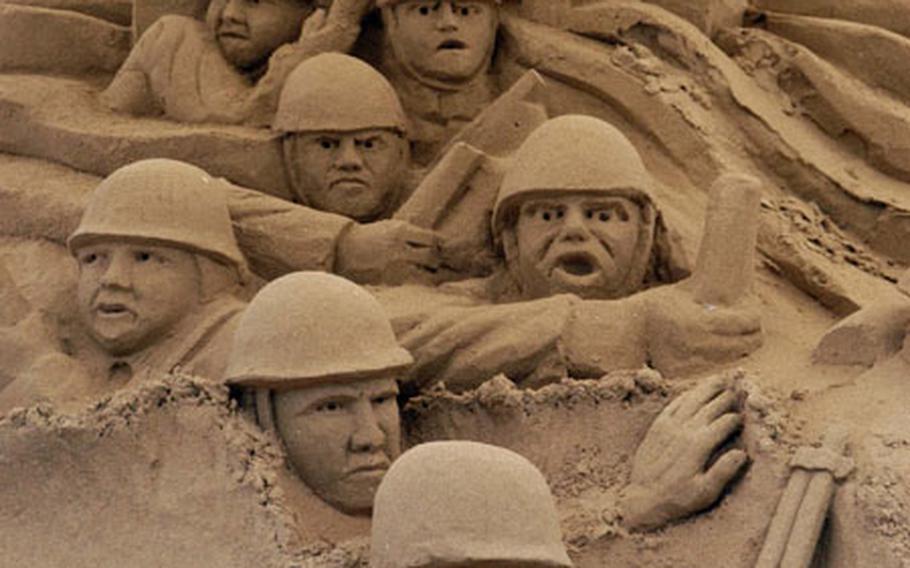 A soldier from the 1st Infantry Division — the Big Red One — leads other soldiers ashore on D-Day in a sand sculpture at Vierville-sur-Mer, France. The sculpture was around 10 feet high, with some of the figures life-size.
