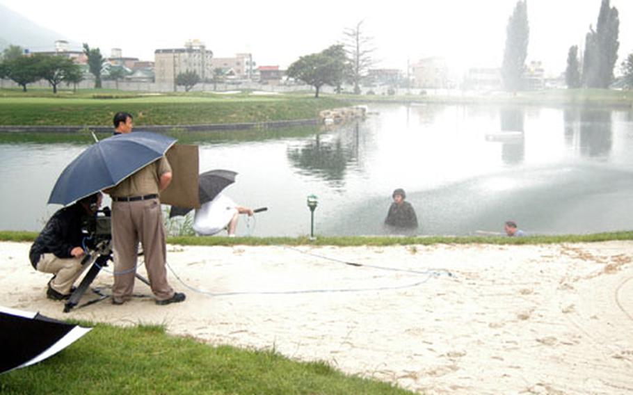 Waist-deep in the island hole at Camp Walker Golf Course in Taegu, South Korea, Army Col. James M. "Mike" Joyner films a TV spot with safety tips for Korea&#39;s monsoon season. Visible at right, in pond, is Kevin B. Jackson, Joyner&#39;s public affairs chief.