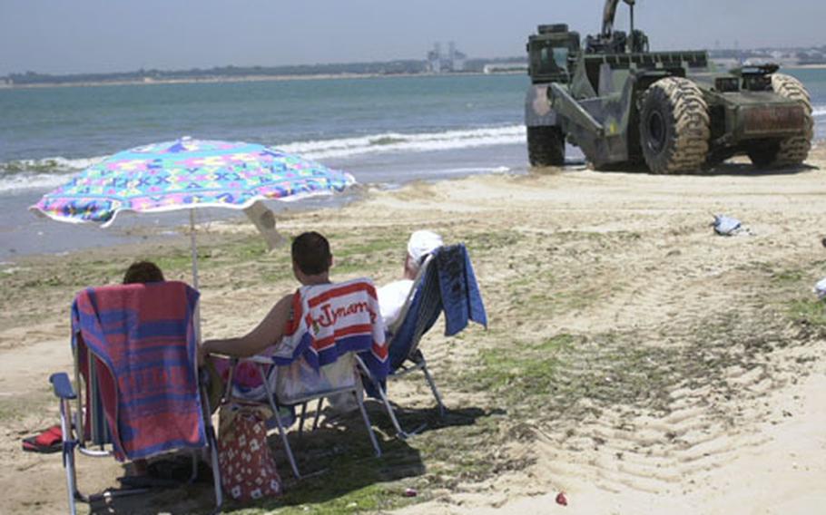 Beach-goers relax and watch a U.S. Navy scraper from Naval Mobile Construction Battalion 74 smooth out the beach in Valdegrana, Spain, on Thursday.