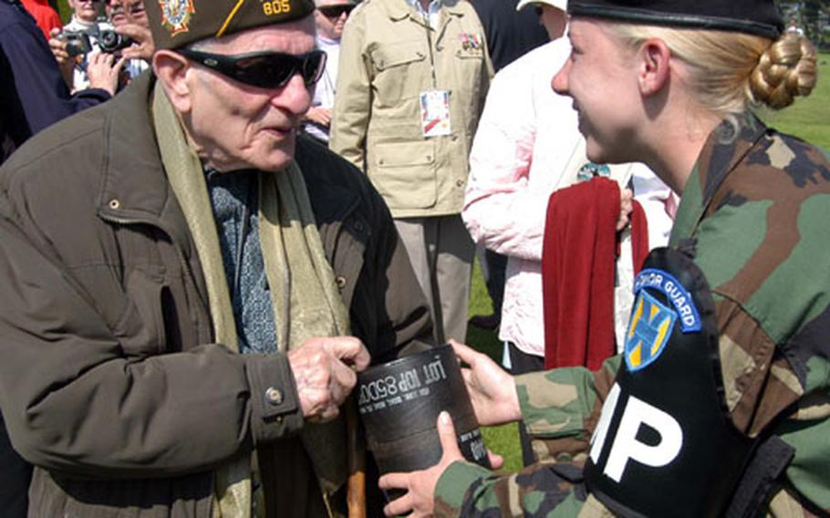 Pfc. Sarah Lutter of the 529th Military Police Company out of Heidelberg, Germany, gives a spent 105 mm shell to veteran Harry Cohen as a souvenir. The 529th passed out the shells they used at Sunday&#39;s 60th anniversary of D-Day ceremony at the Normandy American Cemetery, and the ones spent during rehearsal.