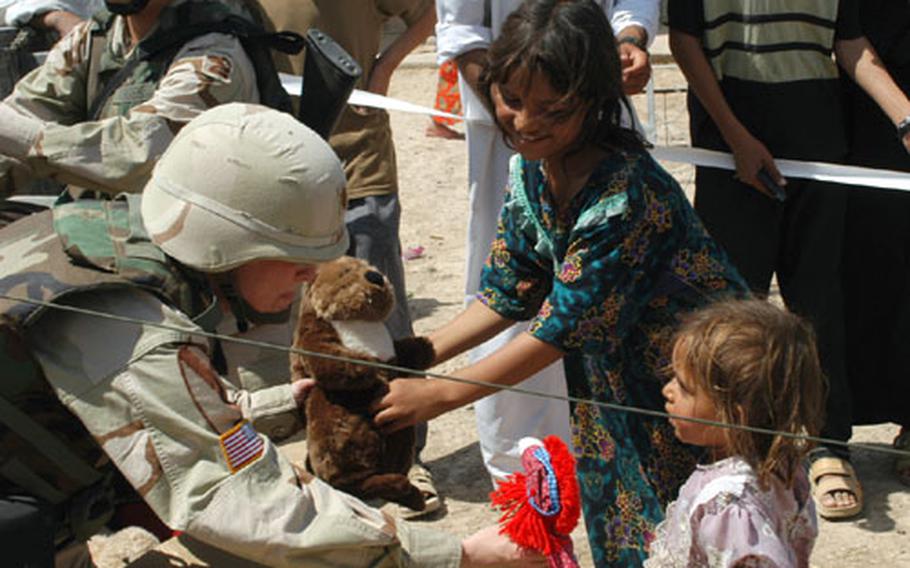 Maj. Juliann Doris, of the 13th Corps Support Command G-5 civil affairs unit, offers dolls to two Iraq girls Monday in the village of Al Fadouz, near Balad, Iraq. Giving gifts to the children of tribes outside of LSA Anaconda helps build better community relations and may stop future attacks on the camp, according to civil affairs officials.
