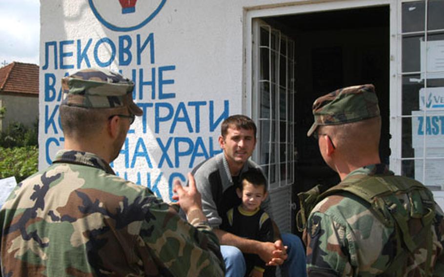 Translator Ardian Kastrati makes a point while asking a question to Slavica Pasjane, a Kosovo Serb, in front of his family&#39;s veterinary clinic in the Serb village of Pasjane on Tuesday. Staff Sgt. Casey Bultman waits for the answer after asking the question. He and other members of the Iowa National Guard conducted a survey of local businesses during one of their regular patrols of the area.