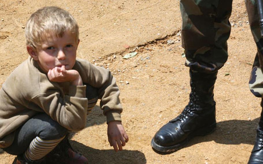 A young Kosovar boy looks up after closely inspecting the boots of Staff Sgt. Casey Bultman during a visit to the boy&#39;s home by the Iowa National Guardsman that took his patrol near the border with Serbia. Bultman was asking the boy&#39;s mother if everything was OK.