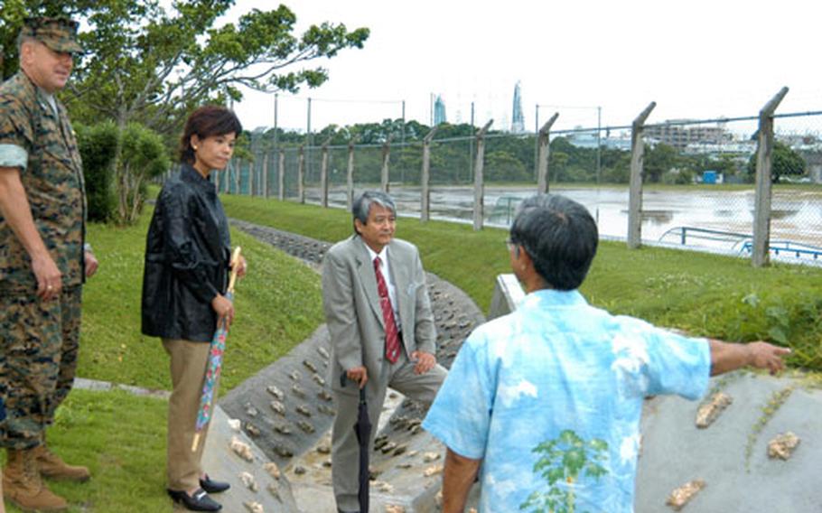 Col. Richard Leuking, commander of Marine Corps Air Station Futenma, left, listens with base community relations specialist Elana Takaho and Hiroshi Higa, director of the Military Affairs Office of Ginowan City, while a representative of the Marines&#39; Facility Engineering Division explains how building a drainage ditch relieved a floding problem at a city elementary school bordering the base.