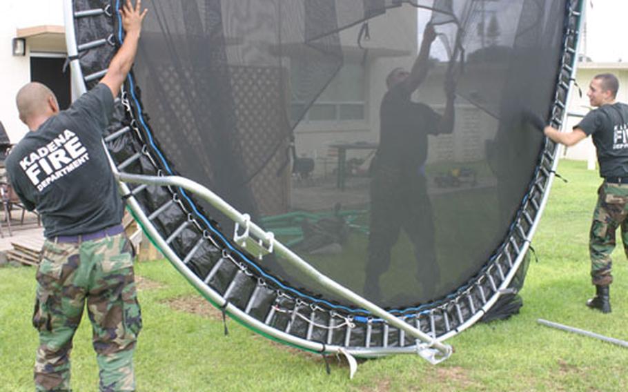 In anticipation of high winds from Super Typhoon Dianmu, Airman 1st Class Gerald Gleason, left, Staff Sgt. Quirino Cabrera (obscured) and Senior Airman Jeremy Camacho, right, of the Kadena Air Base fire department flip Cabrera’s trampoline over and secure it with sandbags Friday.