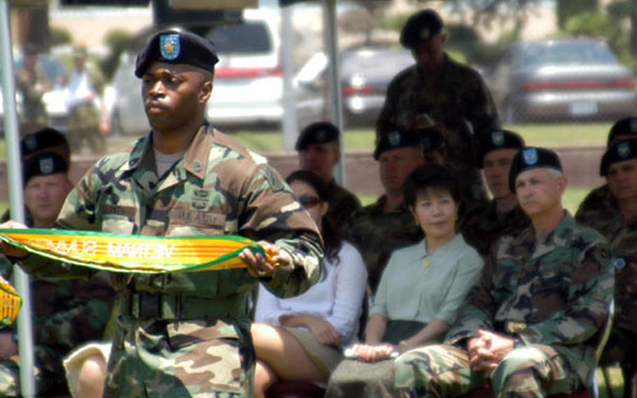 A soldier carries battle streamers to place on the Army flag during a Streamer Ceremony at Camp Zama. Seated in the background is Gen. Elbert N. Perkins who reintroduced this and other ceremonies.