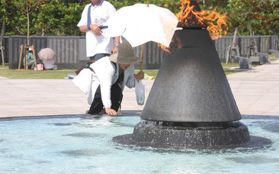 Tamie Toma, 60, visiting the Okinawa Peace Memorial Park in Itoman, dips her hand into a pool of water Wednesday at the edge of the Flame of Peace in the park&#39;s Cornerstone of Peace area. The memorial commemorates the more than 200,000 lives lost in the Battle of Okinawa. The Flame of Peace burns continually.