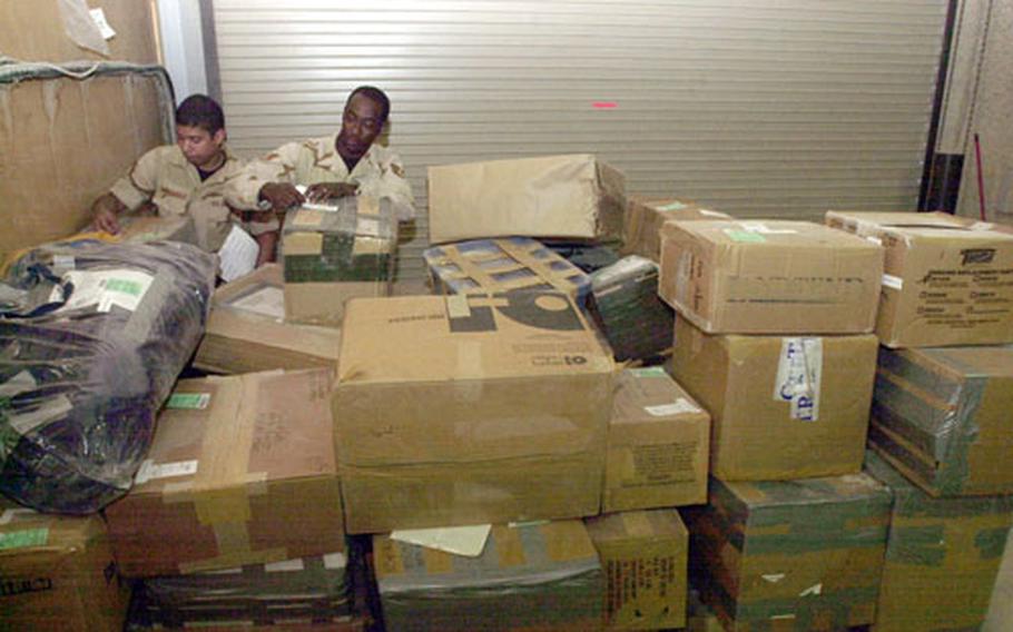 Postal clerks Airmen 1st Class Juan Melendez, left, and Staff Sgt. Albert King, official and registered mail manager, are almost lost behind a stack of boxes. Deployed postal clerks to the Middle East work all aspects at the post offices, not just their normal duties when at their home base.