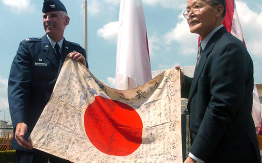 Col Mark Schissler, at left, commander of the 374th Air Wing at Yokota Air Base returns a Japanese flag to Manshichi Saeki during a ceremony in front of the headquarters building. The flag belongs to Ippei Saeki, younger brother of Manshichi, who died fighting against American forces during World War II almost 60 years ago. The flag, which was signed and given to Ippei by his friends and relatives before he died, was brought to the United States after the war. It was traced back to his hometown about 15 miles from Yokota.