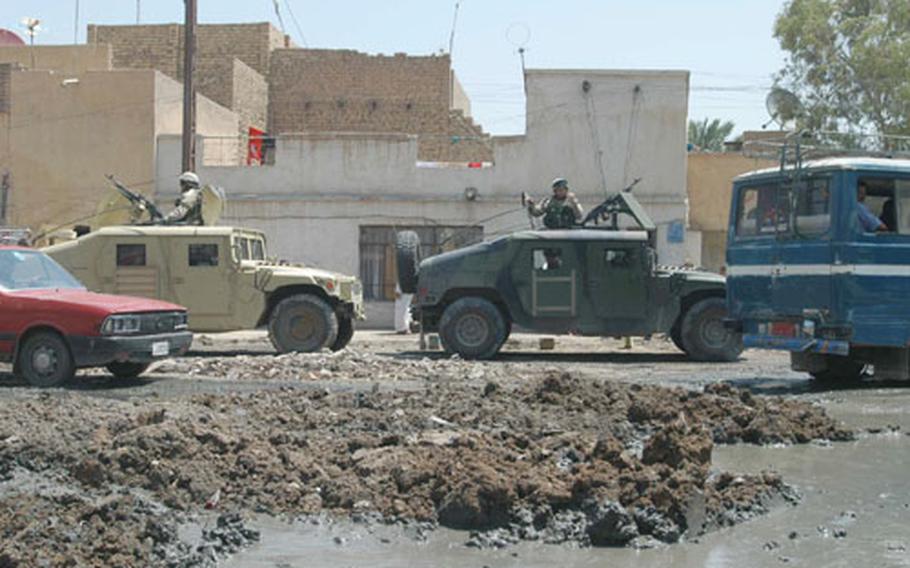 Sewage sits pooled at an intersection in Baghdad&#39;s Zafraniya neighborhood. In the background, soldiers of the 8th Engineer Battalion stand guard while officials look at a construction project for a new sewage system, the first that the area will have in its nearly 40-year history.