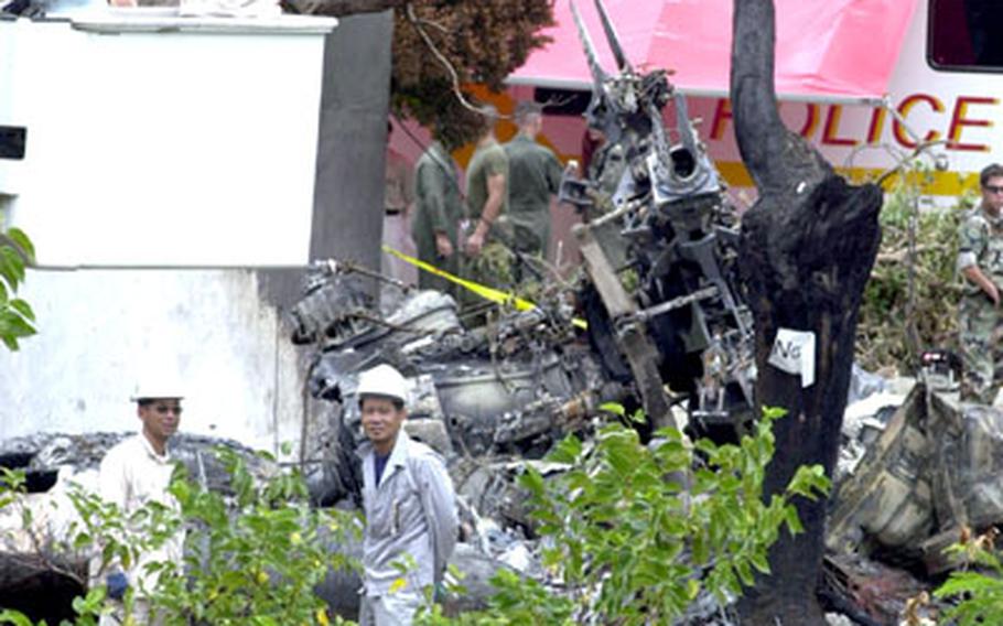 Japanese workers cut down the trees surrounding the wreckage of the Marine Corps CH-53D helicopter that crashed on Okinawa International University grounds.