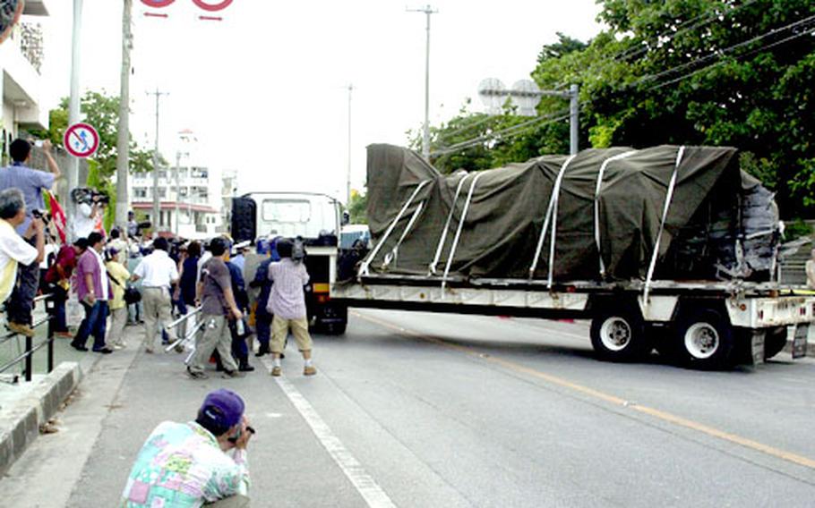 Protestors and media begin to flood the street as the flatbed truck carrying the tail of the CH-53D leaves the grounds of Okinawa International University.