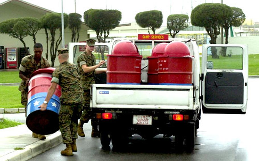 From left, Pfc. Kendrick Harris, 20; Pfc. Stephen Rose, 20; and driver Pfc. Chris Broadstreet, 19, workers from the Camp Foster camp services unit, load trash cans onto a flatbed truck Tuesday, taking precautions for high winds expected from Tropical Storm Megi.