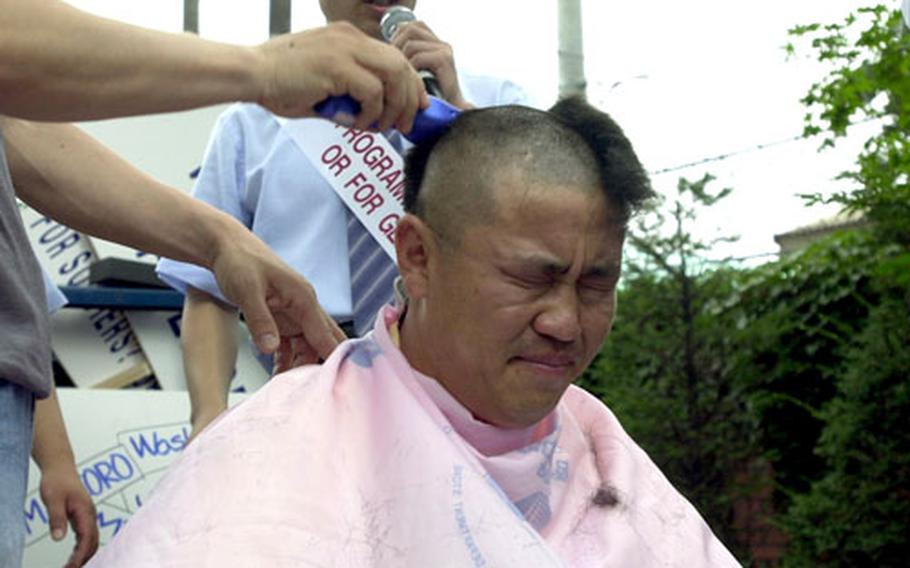 Lim Jong-han, a property owner, winces as other demonstrators protesting a new Army housing program shave his head Tuesday outside the gates of Yongsan Garrison. More than 600 landlords and real estate agents protested the program, which will give landlords a deposit rather than monthly rent, driving down rental profits.