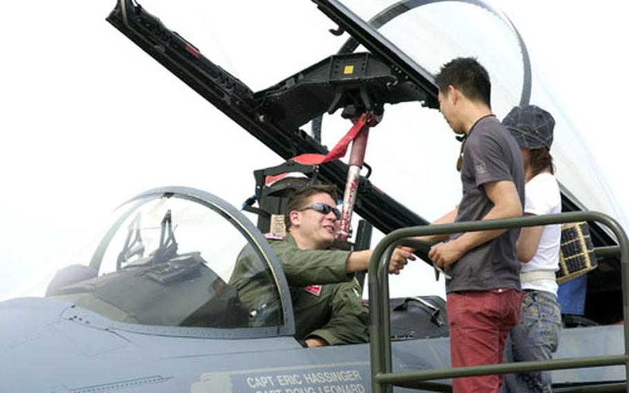 A pilot shakes hands with visitors during the Friendship Day Festival while sitting in the cockpit of an A-10 Thunderbolt at Yokota Air Base.