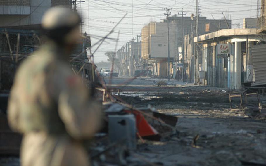 A soldier looks down a Najaf street through a thick web of electrical wires. The wires are a threat to Humvee gunners, as is rebar sticking out from damaged buildings or those which had been under construction before the fighting started. Rebar has also lodged in the tracks of tanks and Bradleys during fights.