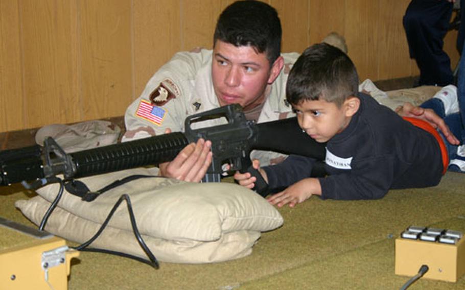 Sgt. John Garcia holds the barrel while his son, Jonathan, takes aim at a small paper target. Sgt. Garcia taught a group of boys the basics of markmanship with this simulator, called the "Weaponeer."