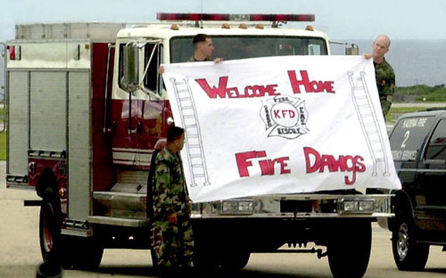 Kadena Air Base fire personnel hold up a sign welcoming home some of their comrades from deployment. They also lined up several trucks and flashed the lights and blew horns and sirens.