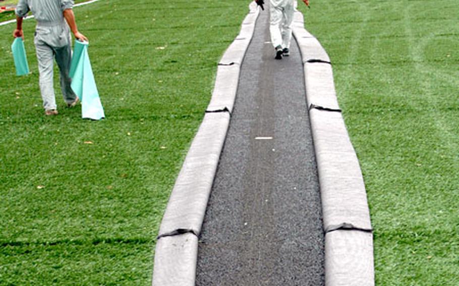 Japanese workers carefully peel back strips of green artificial turf that will later be replaced by white turf that serves as the soccer field boundaries. The field will also have yellow lines for flag football.