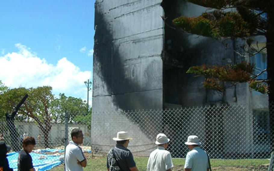 Participants in Sunday&#39;s rally at Okinawa International Univerity stop by the school&#39;s Administration building to view the blackened end where a helicopter clipped the building and crashed, bursting into flames. More than 30,000 people attended the rally, said Ginowan city officials, who hosted the event.