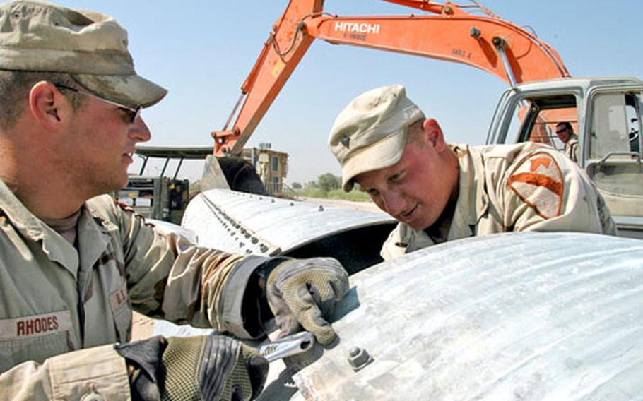 Spc. Matthew Rhodes, left, and Spc. Christian Kessler work to hook together lengths of drainage pipe on Camp Victory. The pipe was eventually used under a new roadway along the camp&#39;s perimeter.