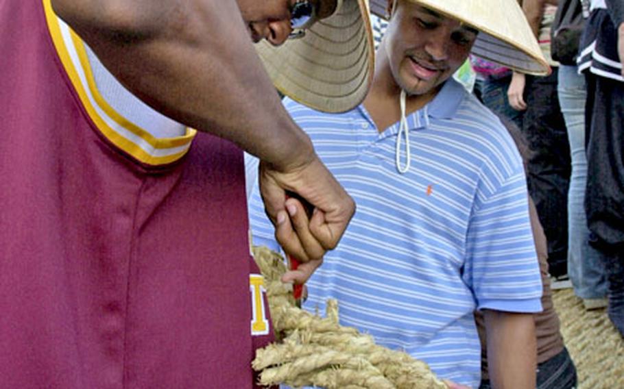 Air Force Staff Sgt. Travis Browner, from the 320th Special Tactics Squadron, cuts a piece off the rope as fellow Staff Sgt. Andre Skeete, from the legal office, looks on. It is said that if you take a piece of rope after the Naha tug-of-war, your family will have good healthy and lots of happiness.