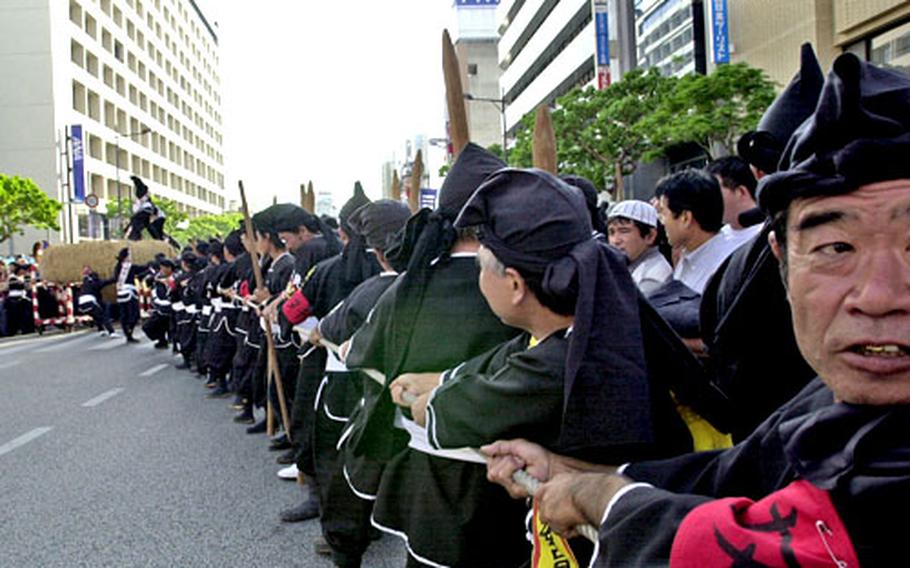 Okinawans dressed in traditional black costumes pull on one half of the giant rope as they prepare to put the two pieces together for the world&#39;s largest tug-of-war.