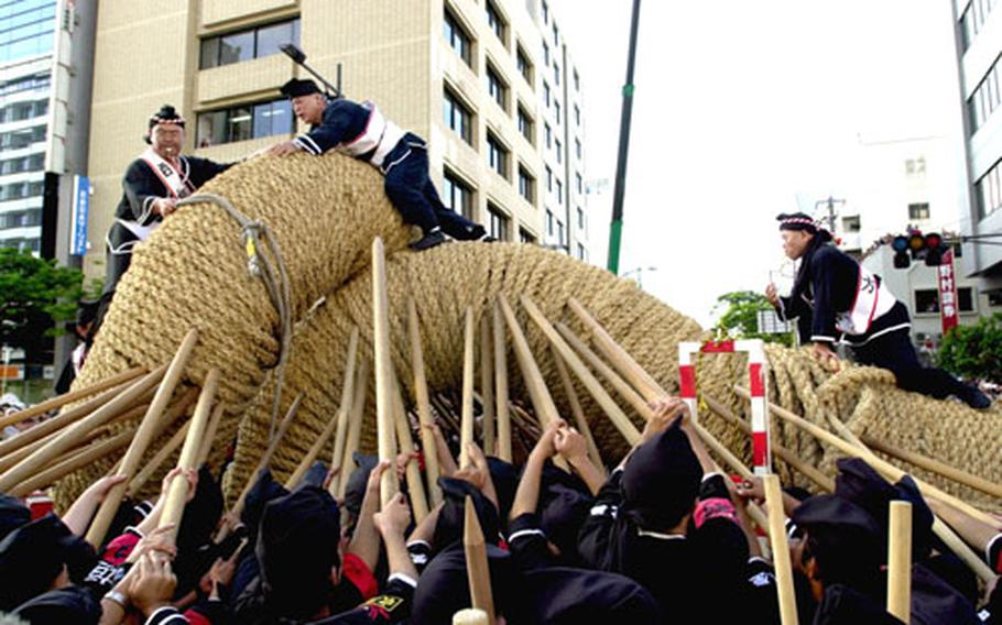 Several men stand atop the two ropes and give orders to those pushing pieces together during the Naha tug-of-war Sunday. Once one end is slipped over the other, a giant wooden peg is inserted to hold the ropes together.