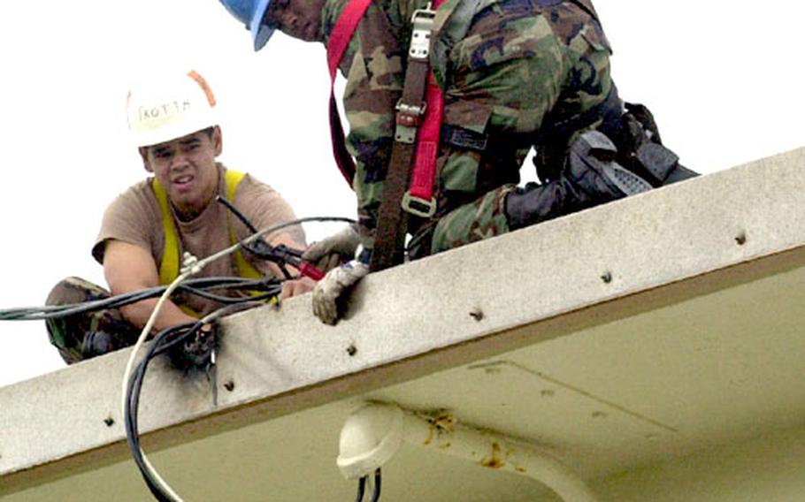 Airman 1st Class Arthur Trotta, left, and Airman Gregory Jenkins repair power lines to a house in Camp Foster&#39;s Futenma housing area Wednesday. The troops from Kadena Air Base&#39;s 18th Civil Engineer Squadron were fixing the lines after they were blown off the building during Typhoon Tokage Tuesday night.