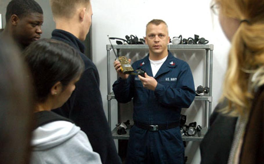 Petty Officer 1st Class Preston Maxwell of the base Aircraft Intermediate Maintenance Department explains a pilot emergency rescue radio to juniors and seniors from Sigonella’s Stephen F. Decatur High School on Tuesday. The students were visiting Maxwell’s department as part of the school’s new career program.