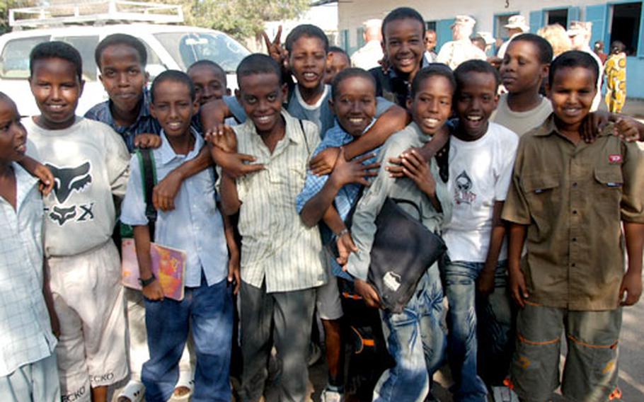 Children pose at a school in Djibouti City, Djibouti, as U.S. troops in the background work out a deal to renovate the buildings. Many of the schools the troops are renovating are so crowded that the children have to attend in shifts, with some going to school in the mornings and others in the afternoons and evenings.