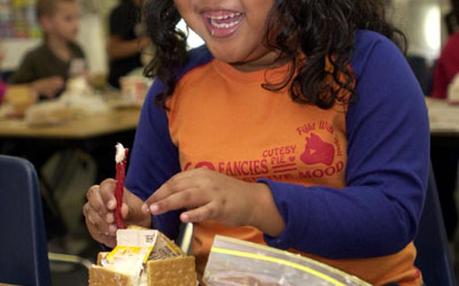 First-grader Tiara Crump is all smiles as she uses a piece of licorice to make a chimney on her gingerbread house during class at Camp Foster’s Zukeran Elementary School on Tuesday on Okinawa. The houses were one of many projects Diane Jackson’s students completed during their “Christmas around the world” celebration.