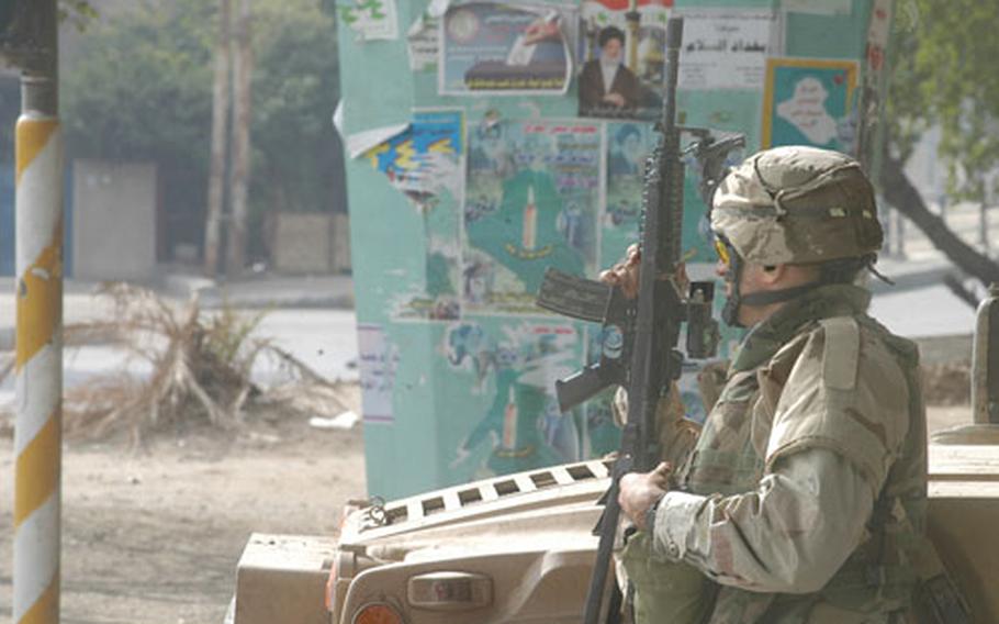 Sgt. Dustin White, medic with 1st Platoon, Company A, 2nd Battalion, 14th Infantry Regiment, stands next to his Humvee on Election Day on Sunday. Posters for the many Iraqi political parties running in the election are pasted on the nearby bridge support.