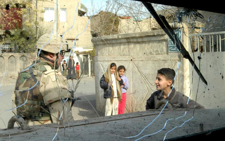 Spc. Michael Johnson talks to an Iraqi boy Sunday as soldiers from Company A, 2nd Battalion, 14th Infantry Regiment, patrol a Baghdad neighborhood during the elections. The picture was taken through Johnson&#39;s Humvee&#39;s cracked winshield, which was damaged that morning when a mortar landed nearby. The attack injured five Iraqis but no soldiers. (enw# 50p cs)