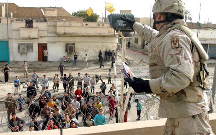 First Lt. R. Dennis Eller, executive officer of Company B, 1st Battalion, 509th Parachute Infantry Regiment, throws packages of colored pencils to youngsters outside the unit&#39;s Geronimo base before Sunday&#39;s elections in Iraq.