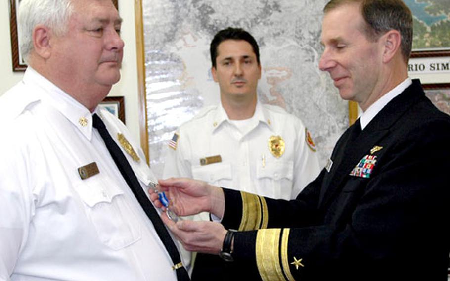 Rear Adm. Frederic R. Ruehe, U.S. Naval Forces Japan commander, right, pins a Navy Superior Civilian Service Award medal to the uniform of Sasebo Fire Chief Richard S. Rhode on Wednesday afternoon. Assistant Fire Chief Jerry Clark looks on during the presentation in the administrative building of the fire department at Sasebo Naval Base.