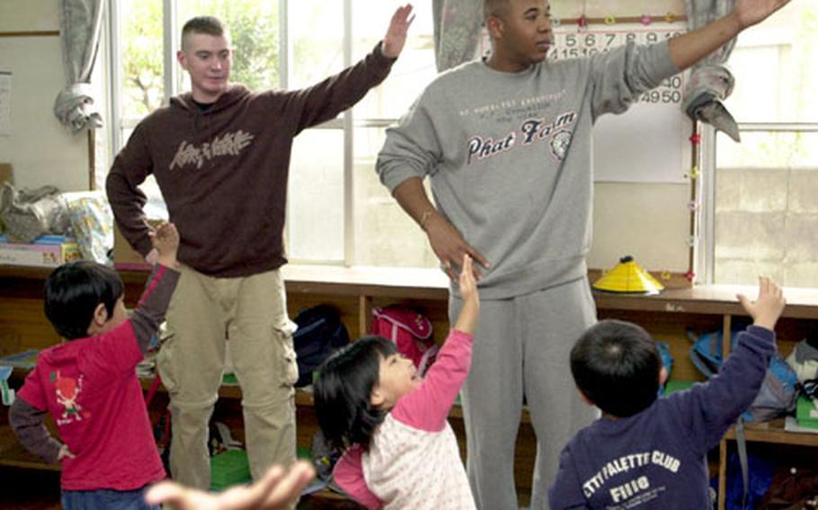 Lance Cpl. Stephen Gomez, right, and Pfc. Class Kyle Roberts get instructions Friday in a traditional Okinawan dance, courtesy of the 3-year-olds at Suginoko Nursery School in Kin, Okinawa. The Marines had earlier taken the children through a round of the “Hokie Pokie.”