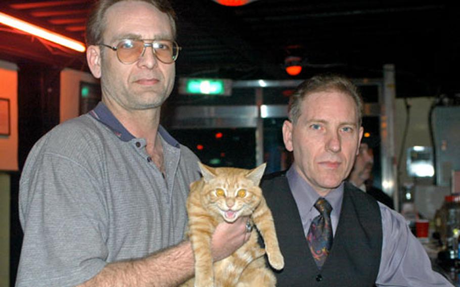 VFW members Doug Tucker, left, Garfield and Dennis Riehley at the Tongduchoen VFW club. Garfield, an orange striped cat who recently saw action in South Korea, is a club regular. VFW members would like Camp Casey soldiers to use the VFW as an alternative to off-base bars.
