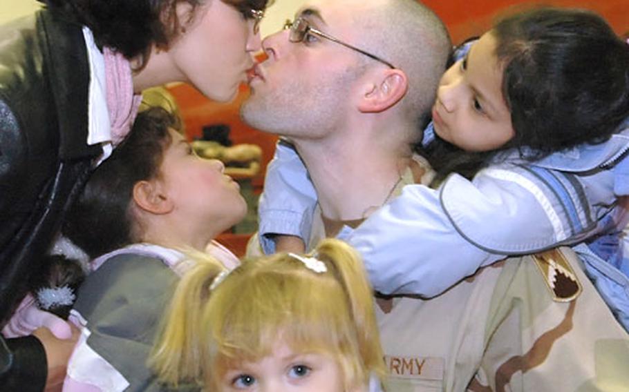 Connie Cart leans over daughter Alaina to give her husband, Sgt. Jason Cart, a kiss while daughter, Jayci, 2, seems distracted at a deployment ceremony for the 44th Signal Battalion in Mannheim, Germany on Wednesday. At right is Alaina&#39;s best friend, Marie.