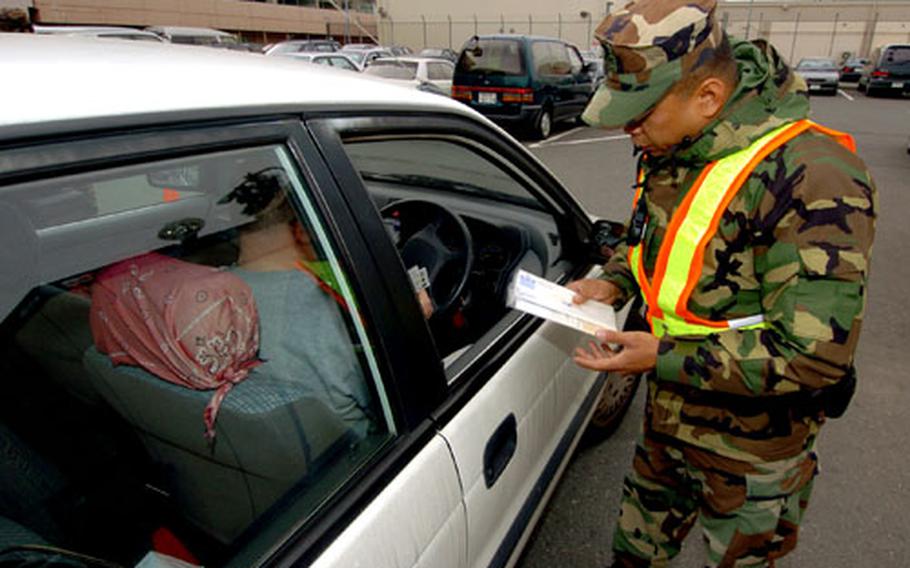 Petty Officer 2nd Class Arnaldo Alejo from Yokosuka Naval Base, Japan, speaks with a driver about his vehicle’s papers Thursday at a base checkpoint. A new Commander, Naval Forces Japan instruction augments driving and vehicle registration rules for Navy personnel in Japan.