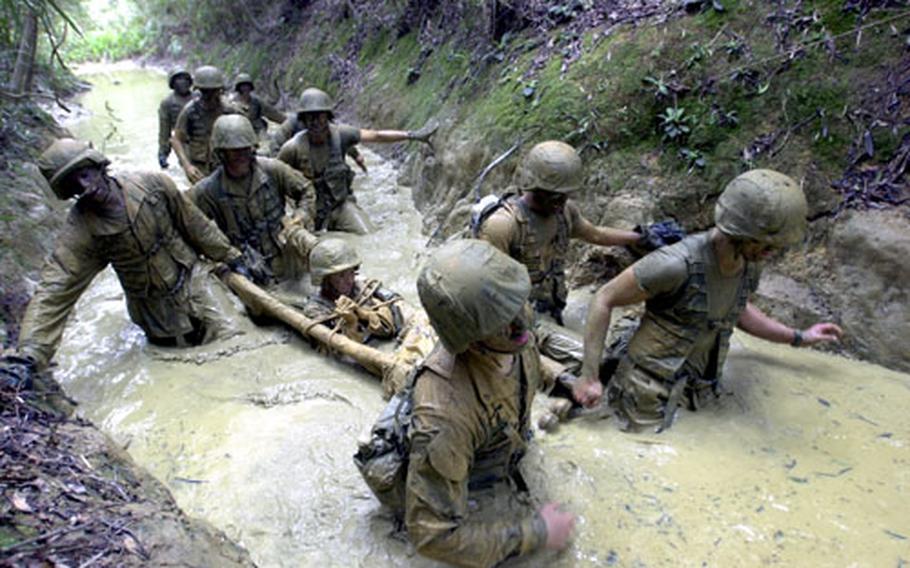 Jungle Warfare Training Center participants struggle to carry a “casualty” through the thick “peanut butter” mud Friday on the JWTC endurance course in northern Okinawa. The course is 3.8 miles long and has 37 obstacles and 14 rappels down cliffs.